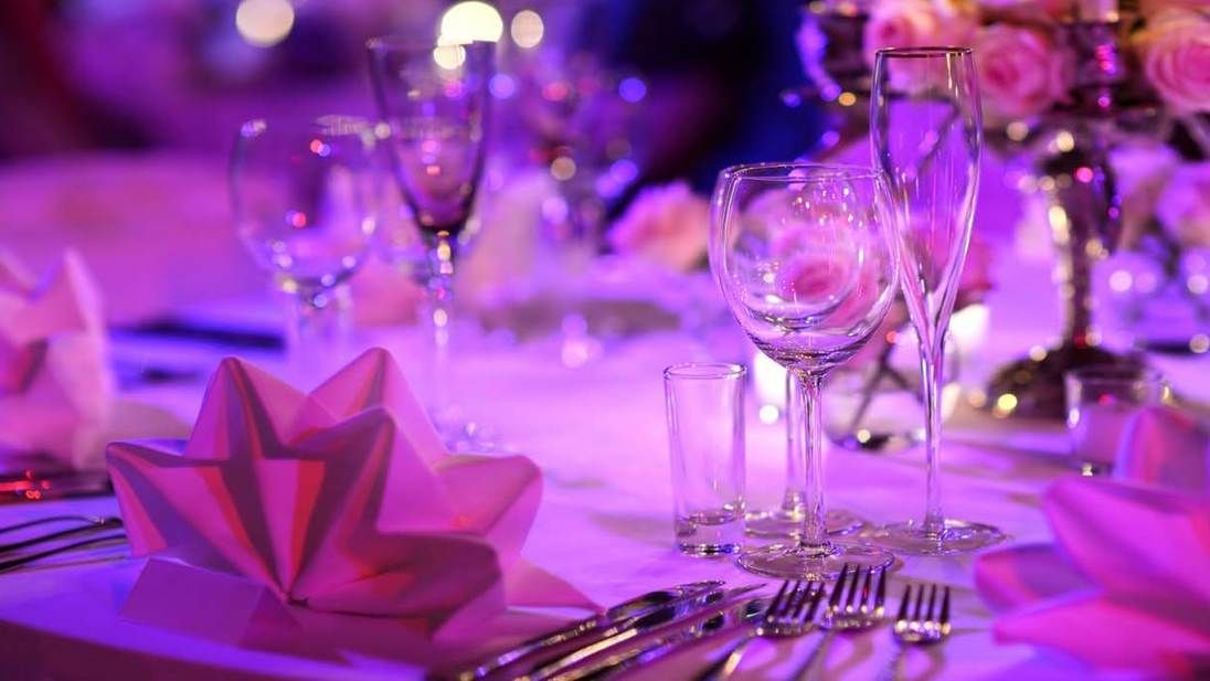 Elegant table setting with glasses and folded napkins under purple lighting at an event or celebration.